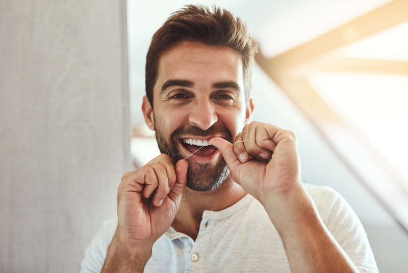 Dental floss, teeth and smile with portrait of man in bathroom for cleaning, morning and oral hygiene. Happy, cosmetics and health with face of person